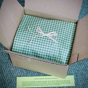 Peut inclure: Une bo&icirc;te en carton avec un papier de soie &agrave; carreaux verts et blancs. La bo&icirc;te est ouverte et le papier de soie est visible. Une petite carte verte et blanche avec le texte "Granny's Garden Adjustable Fedorable" est visible dans le coin inf&eacute;rieur droit de l'image. Le texte sur la carte indique : "La taille de votre Fedorable peut &ecirc;tre facilement ajust&eacute;e. Faites simplement glisser le bandeau vers la droite jusqu'&agrave; ce que la partie velcro apparaisse sous le bandeau crois&eacute;. D&eacute;faites le velcro, (&eacute;tirez le chapeau si n&eacute;cessaire) et refixez-le pour rendre le bandeau jusqu'&agrave; 3/4" plus petit ou plus grand. Ensuite, glissez-le &agrave; nouveau sous le bandeau crois&eacute; (vous devrez peut-&ecirc;tre pincer l&eacute;g&egrave;rement le bandeau pour le faire passer sous le bandeau crois&eacute;)"