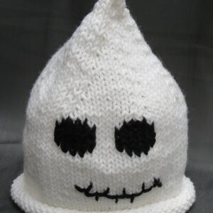 May include: White knitted hat with a ghost face design. The ghost has black eyes and a stitched mouth.