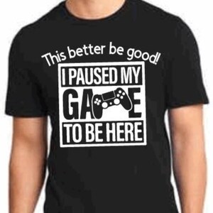 May include: Black t-shirt with white text that reads "This better be good! I paused my game to be here."  A white video game controller icon is in the middle of the text.