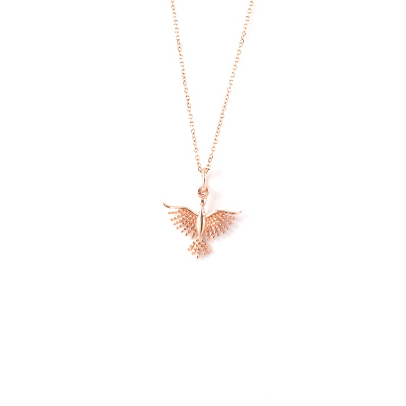 May include: A delicate gold necklace with a small, detailed bird pendant. The bird has spread wings and is made of a textured metal.