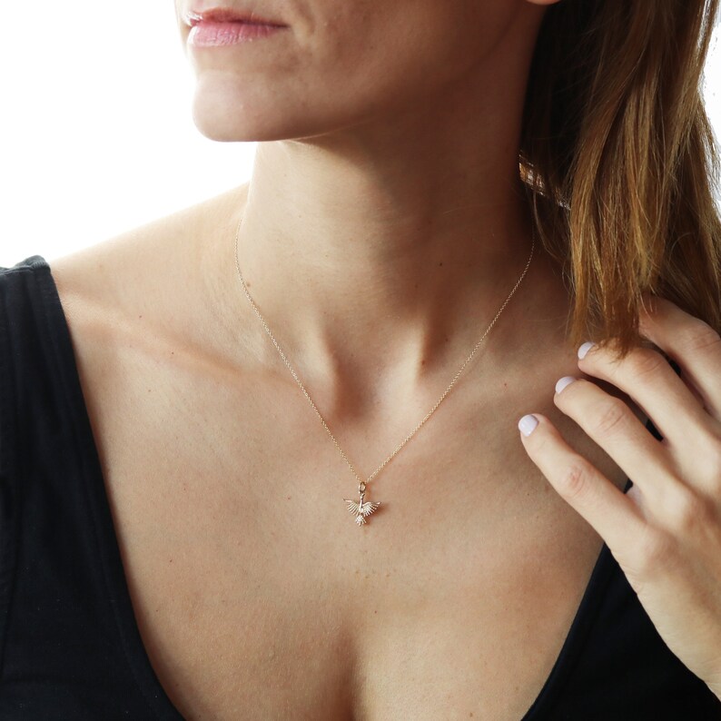 May include: A gold chain necklace with a small hummingbird pendant. The hummingbird is made of gold and has a clear crystal body.