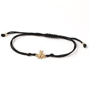 May include: A black string bracelet with a gold frog charm. The bracelet is adjustable and has a simple design.