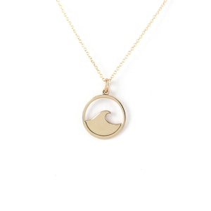 Puede incluir: Un collar de oro con un colgante circular que presenta un diseño de ola recortada.