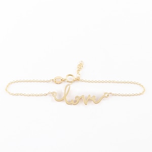 Könnte beinhalten: Ein goldenes Kettenarmband mit einem "Love"-Anhänger in Schreibschrift. Das Armband besteht aus einer zarten Kette und hat einen Karabinerverschluss.