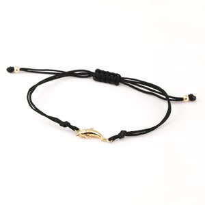 Puede incluir: Un brazalete de cuerda negra con un dije de delfín dorado. El brazalete es ajustable con un nudo deslizante.