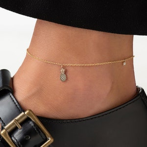 May include: Gold ankle chain with a small pineapple charm and a single pearl accent.