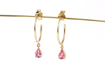 May include: Gold hoop earrings with a dangling pink pear-shaped gemstone.