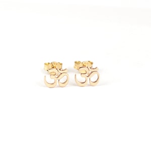 May include: A pair of gold Om symbol stud earrings. The earrings are small and delicate, and they are perfect for everyday wear.
