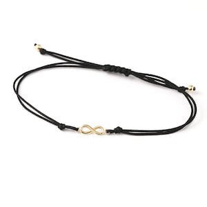 Könnte beinhalten: Ein schwarzes Armband aus Schnur mit einem goldenen Unendlichkeits-Anhänger.