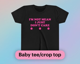 Może przedstawiać: Czarny dziecięcy t-shirt lub crop top z różowym tekstem, który brzmi "I'm not mean I just don't care" z trzema różowymi gwiazdkami pod tekstem.