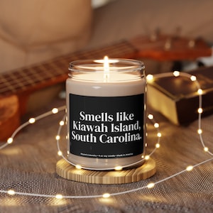 May include: A brown soy candle in a clear glass jar with a black label that reads "Smells like Kiawah Island, South Carolina."  Mo's Laundry 9 oz soy candle - Made in America.