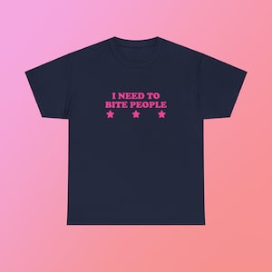 May include: A navy blue t-shirt with the text "I NEED TO BITE PEOPLE" in pink letters and three pink stars below the text.