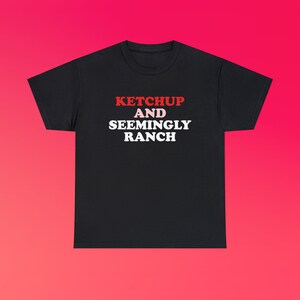 May include: Black t-shirt featuring the text "KETCHUP AND SEEMINGLY RANCH" in red and white. The top has a round neck and short sleeves. The background is a gradient of pink and red.