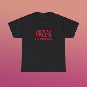 Può includere: T-shirt nero con la scritta rossa "I wish I had serotonin instead of a huge cock." La maglietta è a girocollo e sembra essere realizzata in un materiale morbido. Il testo è centrato sulla parte anteriore della maglietta.