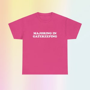 May include: Pink t-shirt with white text that reads "Majoring in Gatekeeping".