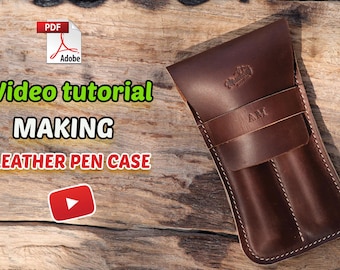 May include: A dark brown leather pen case with two vertical slots, a flap closure, and the embossed initials AM. The image includes text reading Video tutorial MAKING LEATHER PEN CASE, a PDF icon, a YouTube play button, and a Munkong Handcraft logo.