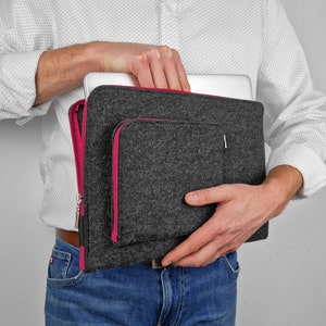 May include: A grey felt laptop sleeve with a pink zipper and a pink pocket. The sleeve is being held by a person.