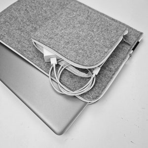 Light grey felt laptop sleeve with front pocket opened. Charger and wires in front pocket. Laptop half out of the sleeve.