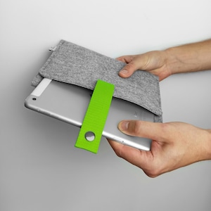 Könnte beinhalten: Eine graue Filz-Tablethülle mit einem leuchtend grünen Riemen und einem Druckknopfverschluss. Die Hülle hält ein silbernes Tablet.