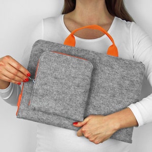 Può includere: Una custodia per laptop in feltro grigio con cerniera e manico arancioni. La custodia ha una tasca più piccola in feltro grigio sul davanti.