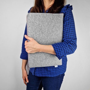 Woman hilding light grey felt laptop case with maroon zipper.