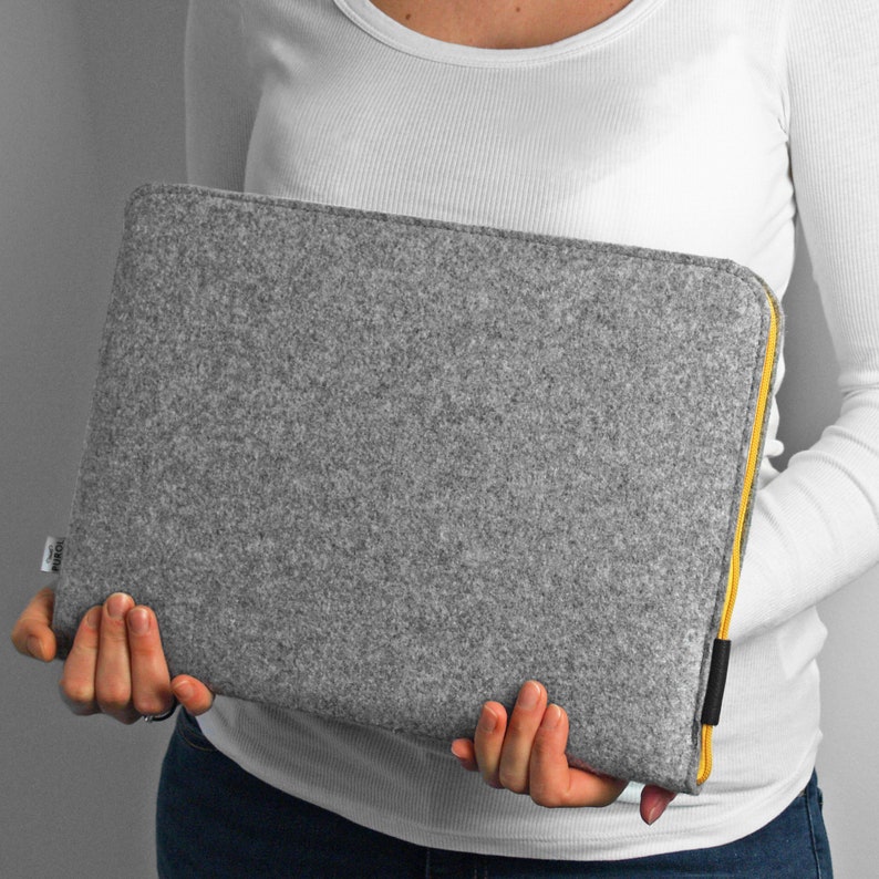 Women holding light grey felt laptp sleeve. Yellow zipper and black synthetic material at the end of the zipper. Zipper opens on the top and one side. Easly fit the laptop in the case.