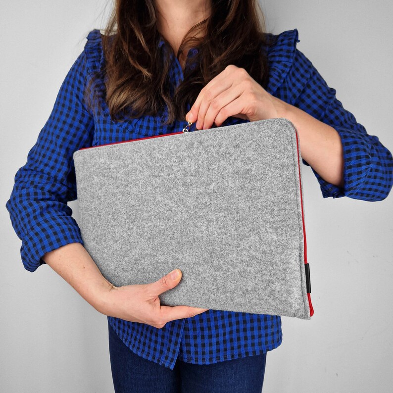 Woman holding light grey felt laptop case with red zipper, Zipper half open.