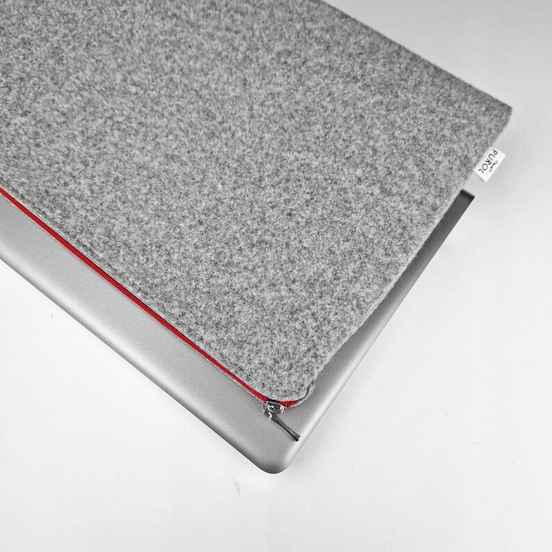 Light grey felt laptop case lying on the silver laptop, red zipper and silver zipper ending.