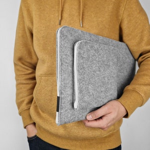 Different angle, man holding light grey felt cover with additional pocket for wires sewn on the front of the sleeve.