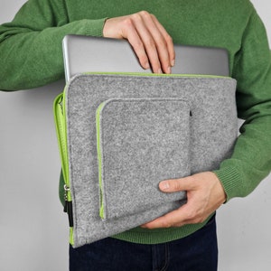Man holding 15 inch laptop half inside the felt sleeve. Green zippers open on the top and side of the sleeve and pocket.