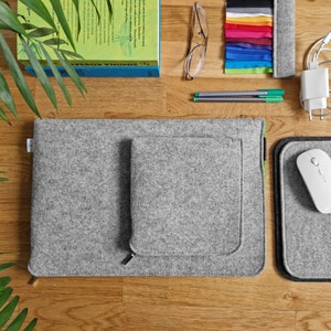 Light grey felt sleeve lying on the wooden table next to felt mouse pad and some books.