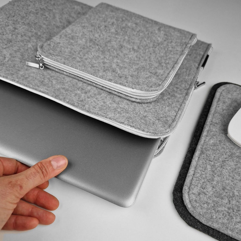 Silver 15 inch laptop half out of the light grey felt sleeve. Lying on the table next to mouse pad.