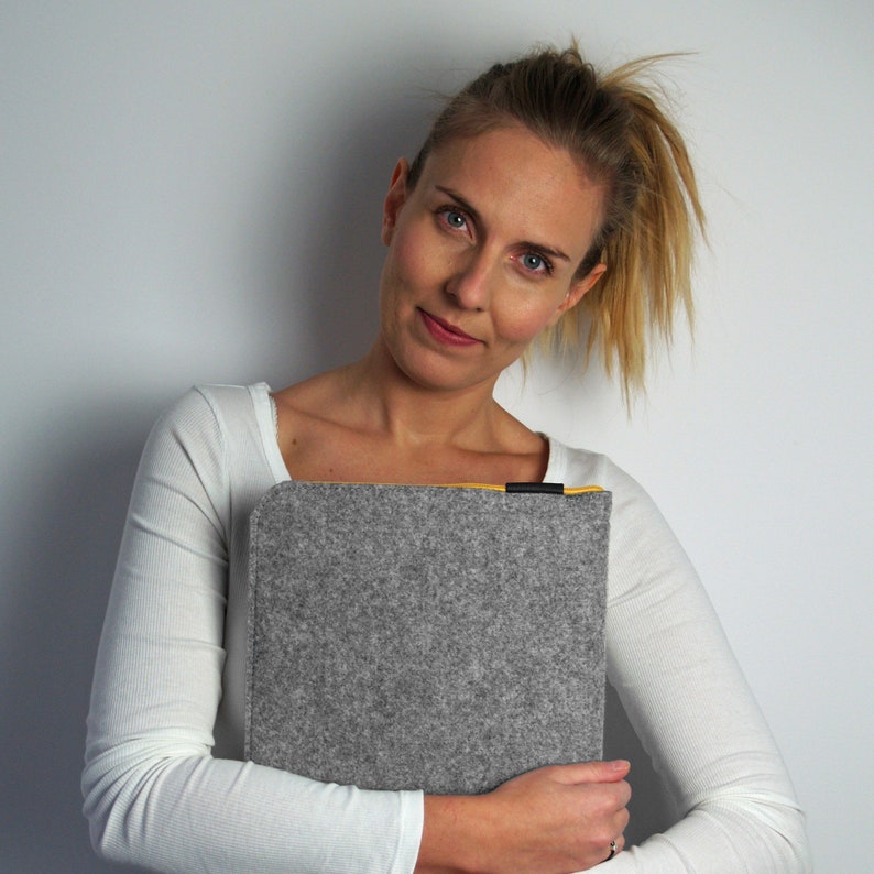 Women holding light grey felt laptp sleeve. Yellow zipper and black synthetic material at the end of the zipper. Zipper opens on the top and one side. Easly fit the laptop in the case.