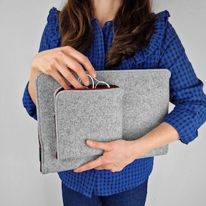Woman holding light grey flet laptop cover. Maroon zippers. Front pocket for charger, wires or mouse. Woman takes out wires from the front pocket.