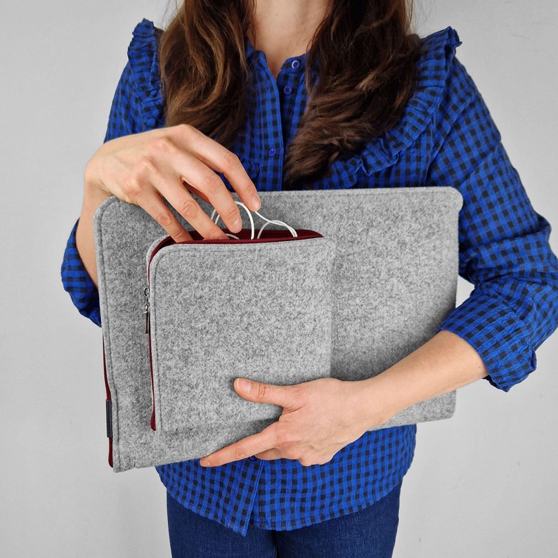 Woman holding light grey flet laptop cover. Maroon zippers. Front pocket for charger, wires or mouse. Woman takes out wires from the front pocket.