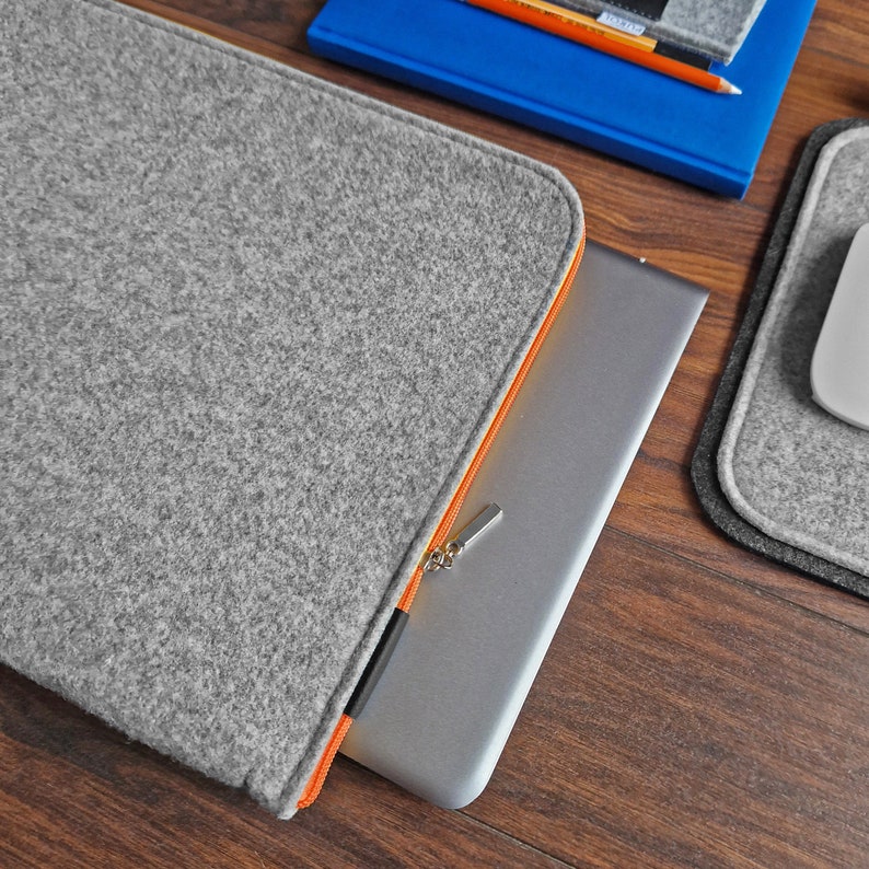 Light grey felt laptop sleeve with orange zipper. 15 inch laptop lying next to felt mouse pad and felt key ring.