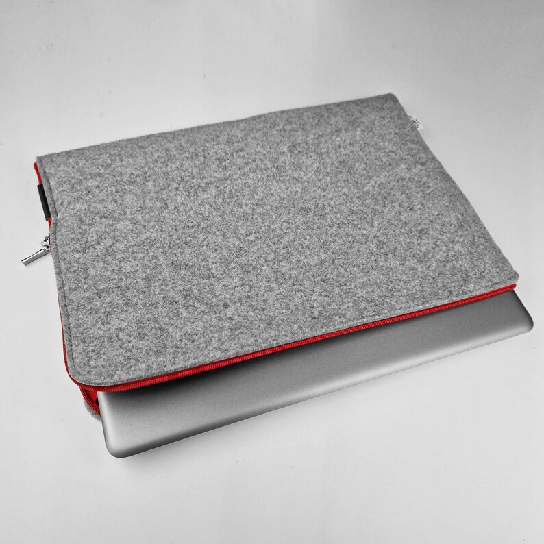 Light grey felt laptop sleeve with red zipper, cover lying flat with laptop half out