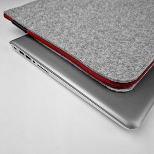 Felt laptop case lying flat on closed laptop. Maroon zipper, zoom on the corner of the sleeve.