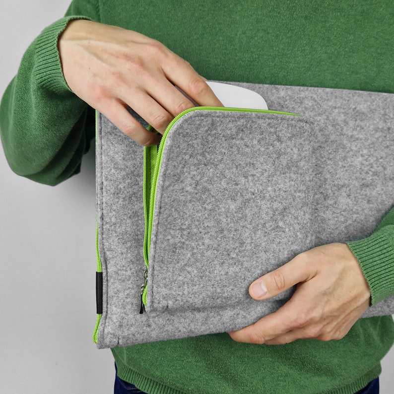 Man holding flet sleeve with front pocket opend. Green zippers.