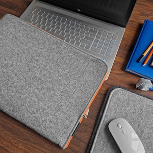 Light grey felt laptop sleeve with orange zipper. 15 inch laptop lying next to felt mouse pad and felt key ring.