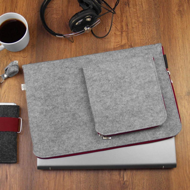 Felt laptop case on the wooden table. Front pocket for wires sewn on the sleeve. Maroon zippers.