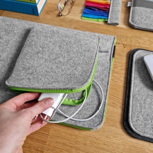 Light grey felt sleeve lying on the wooden table next to felt mouse pad and some books. Front pocket for charger opend.
