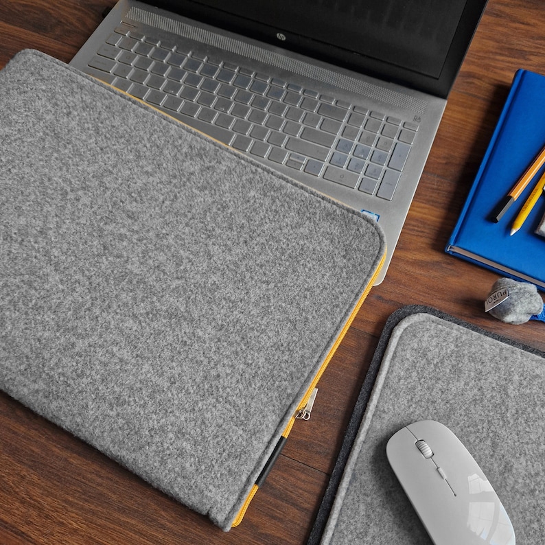 Light grey felt sleeve with yellow zipper on the table next to 15 inch laptop and felt mouse pad.