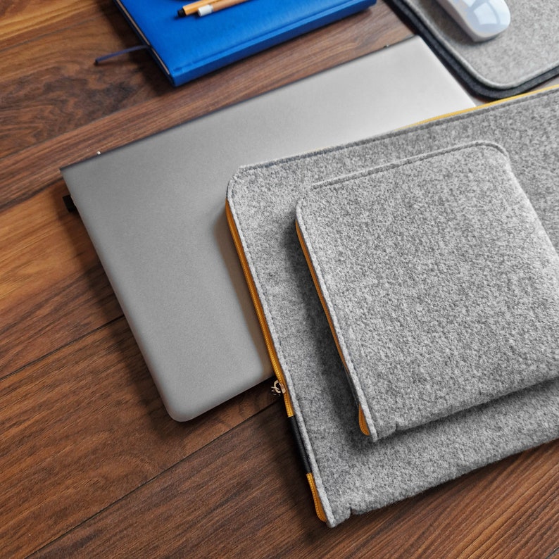 Felt laptop case with pocket for wires sewn on the main part of the sleeve. 15 inch laptop lying on the desk next to sleeve. Case with Yellow zipper.