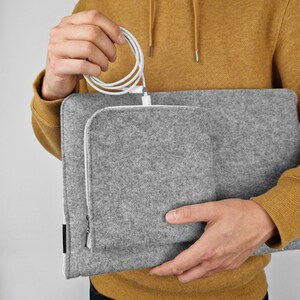 Man holding felt sleeve for laptop. Cables in the front pocket with white zipper.