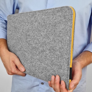 Men holding light grey felt laptp sleeve. Yellow zipper and black synthetic material at the end of the zipper. Zipper opens on the top and one side. Easly fit the laptop in the case.