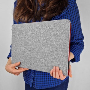 Woman hilding light grey felt laptop case with maroon zipper.