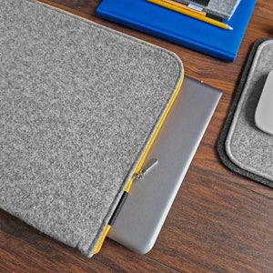 Light grey felt sleeve with yellow zipper on the table next to 15 inch laptop and felt mouse pad.