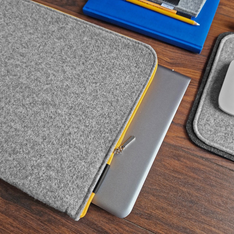 Light grey felt sleeve with yellow zipper on the table next to 15 inch laptop and felt mouse pad.