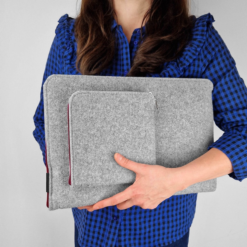 Woman holding light grey flet laptop cover. Maroon zippers. Front pocket for charger, wires or mouse.